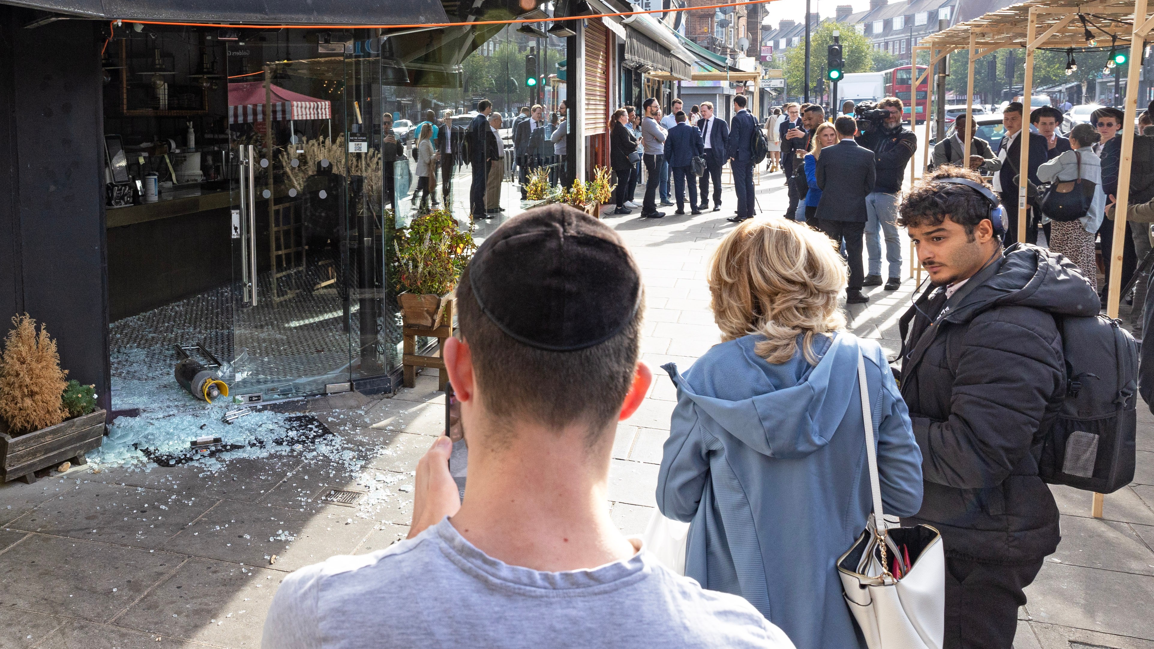 A man wearing a kippah takes a picture of damage caused when a gas canister was thrown through a kosher shop door in Golders Green, north London, on October 9