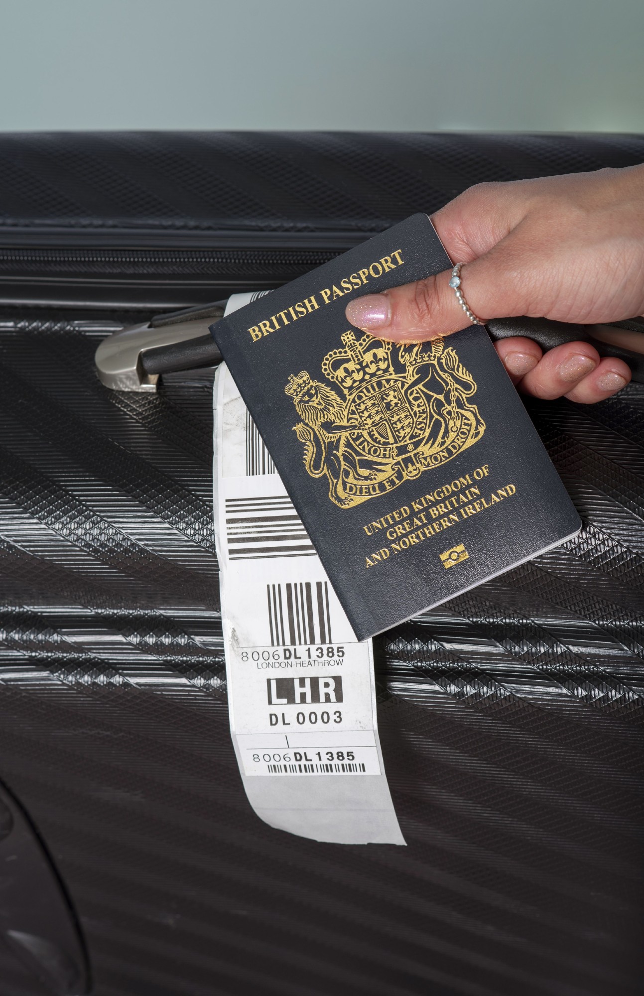 hand holding a UK passport by their suitcase