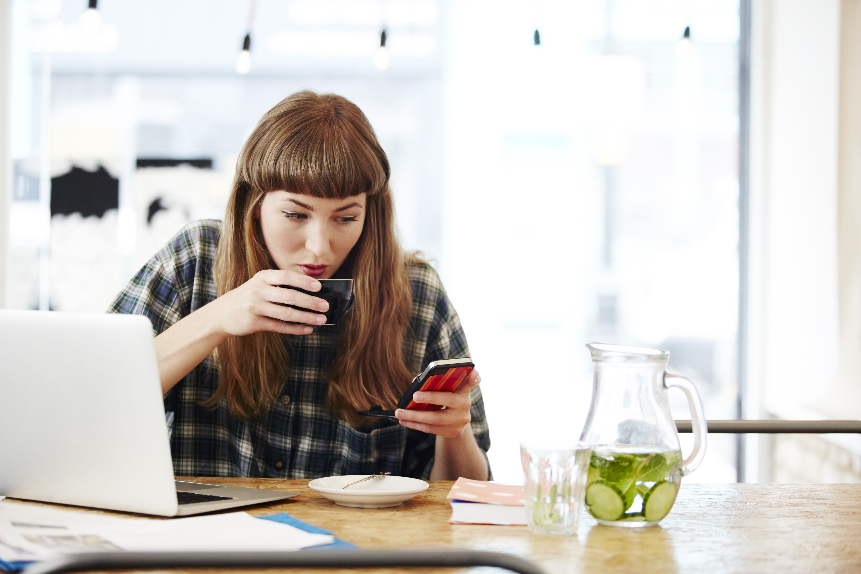 Young woman sipping a coffee, checking her phone for the best savings rates