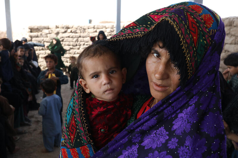 A mother wraps a shawl around her child, who she is holding.