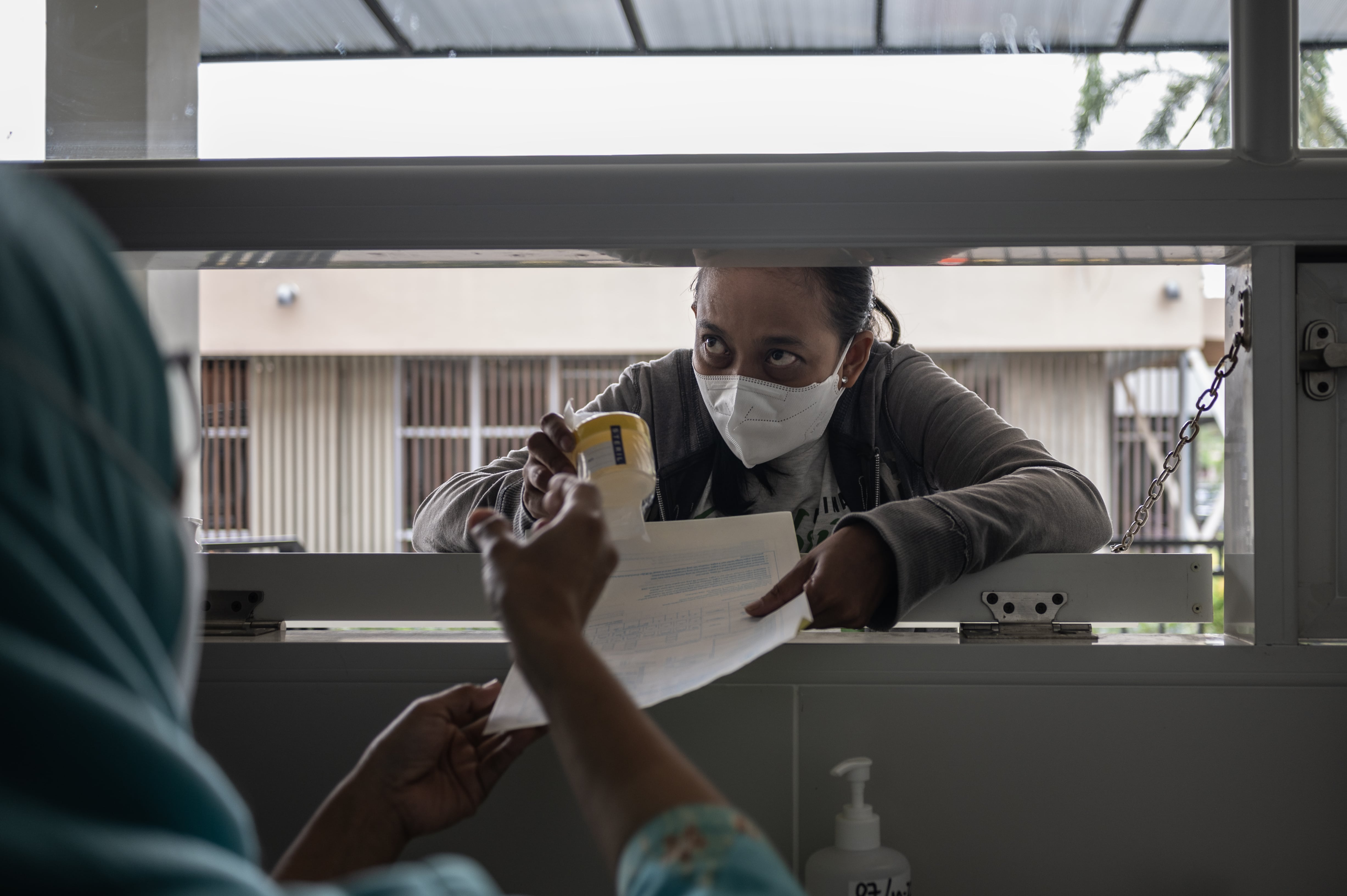 Paran, a survivor of drug-resistant TB, wearing a medical mask taking a form at a service window.