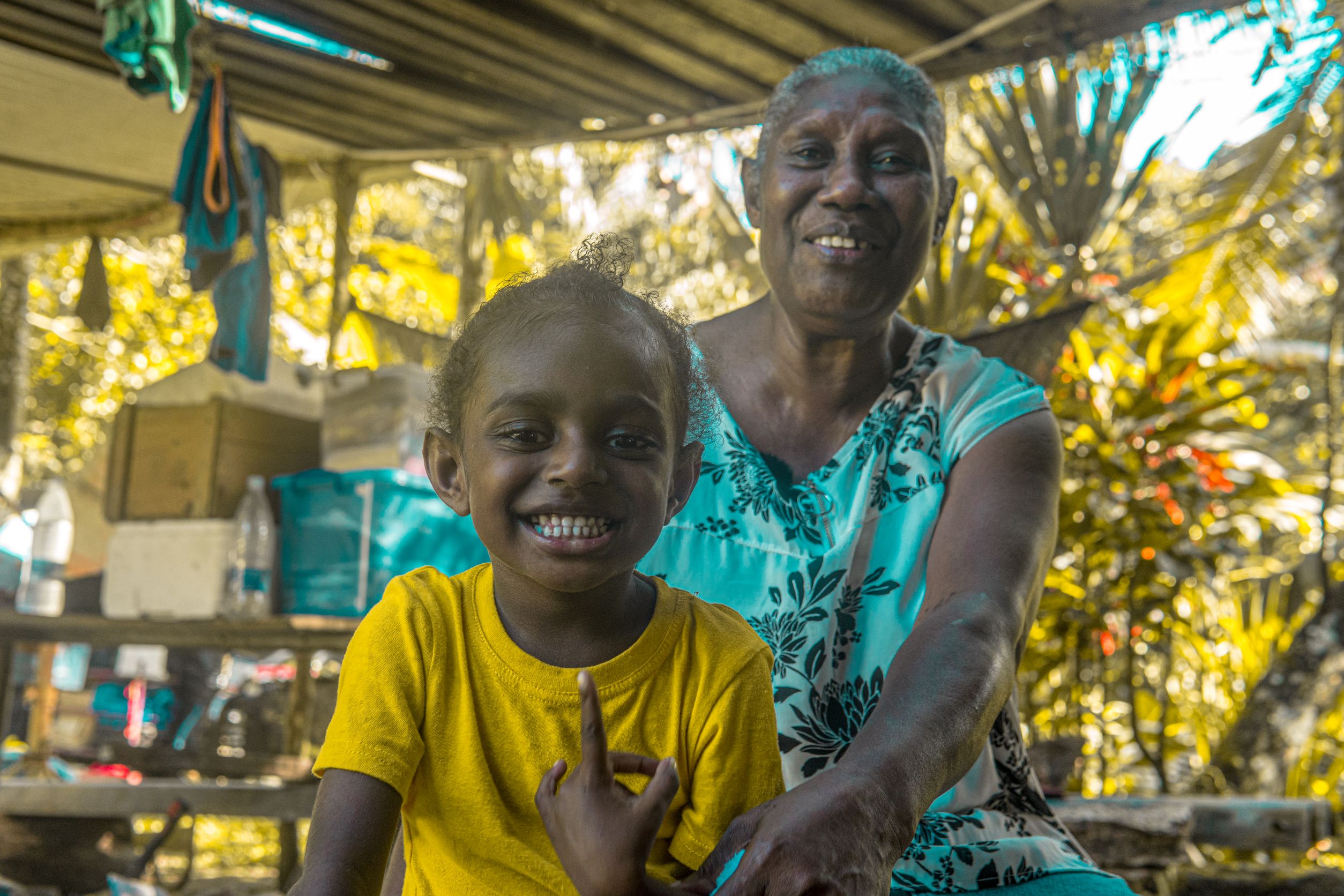 A young girl in Vanuatu smiles to show her teeth with her grandmother