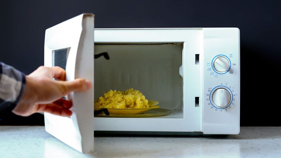 A plate of food in a microwave with the door being opened (Credit: Getty Images)
