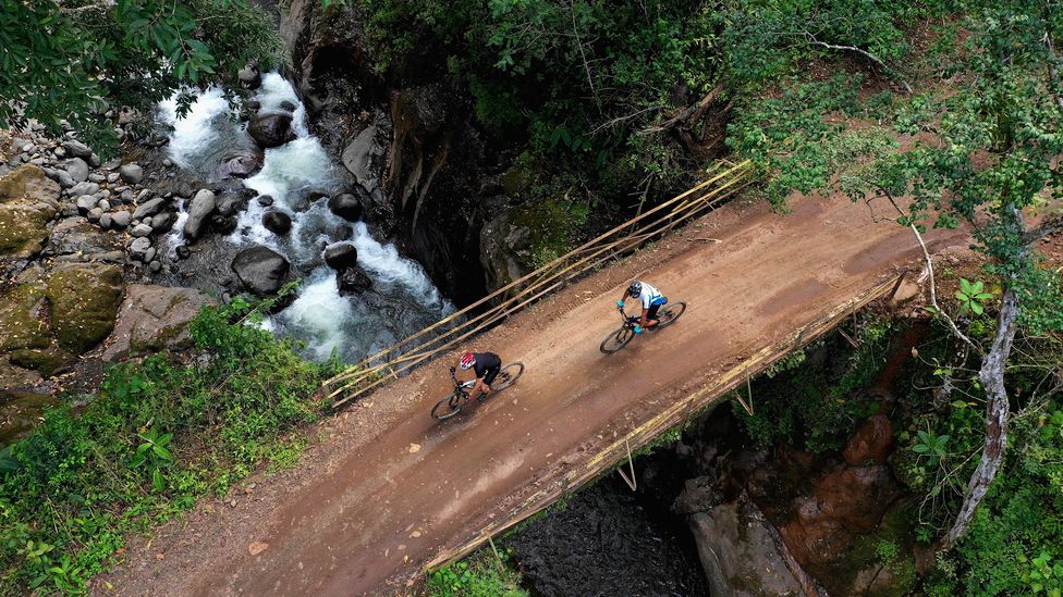 Cyclists pass over a bridge in a Costa Rican forest (Credit: Getty Images)