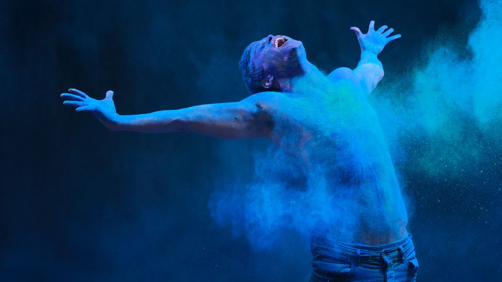 Man stretching out arms is covered in blue powder (Credit: Henrik Sorensen/Getty Images)