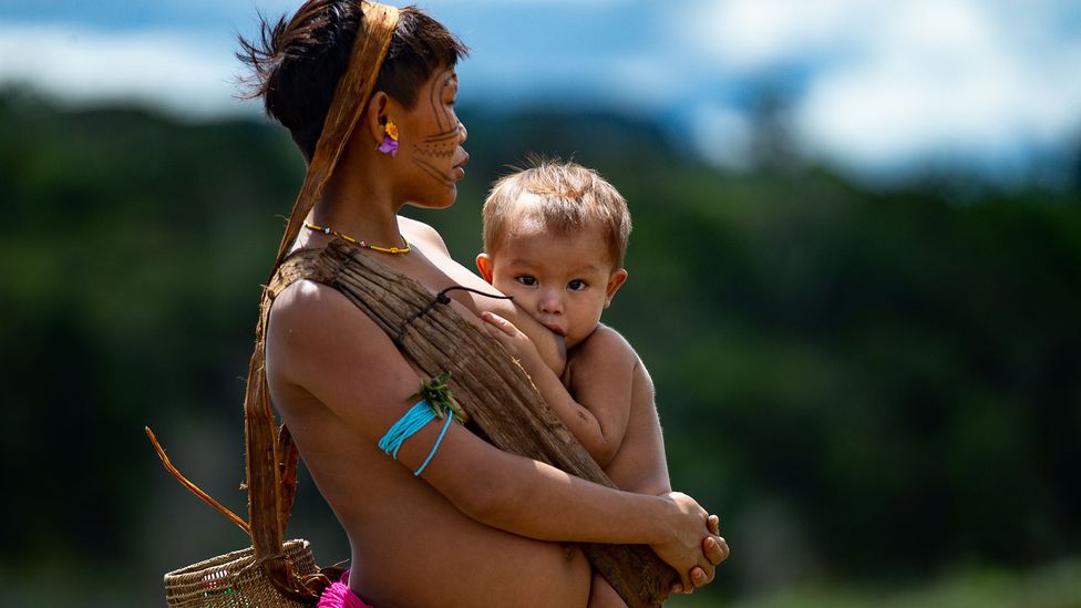 A Yanomami mother breastfeeds her baby as she waits at a health care centre in Brazil (Credit: Andressa Anholete / Getty Images)