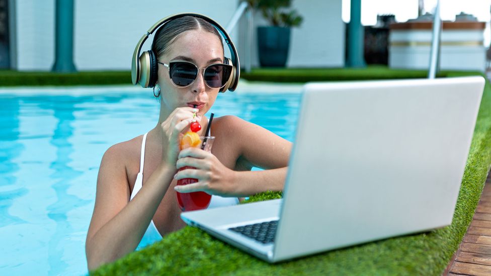 Young worker in front of her computer poolside with a cocktail