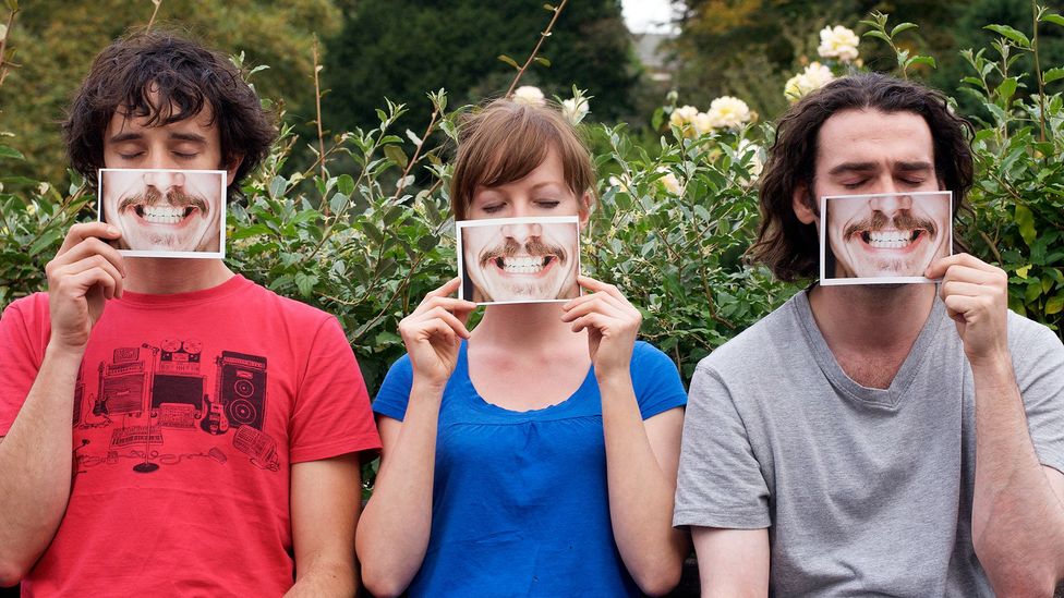 Two men and a woman hold up photographs of a mouth in front of their faces (Credit: Getty Images)